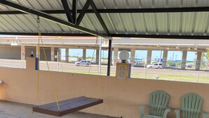A covered outdoor seating area with a swing, green and white plastic chairs, and a concrete floor. - Executive Inn and Suites (Mission)