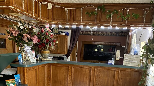A reception area with a wooden counter, a large floral arrangement, and a sign indicating the executive suite. - Executive Inn and Suites (Mission)