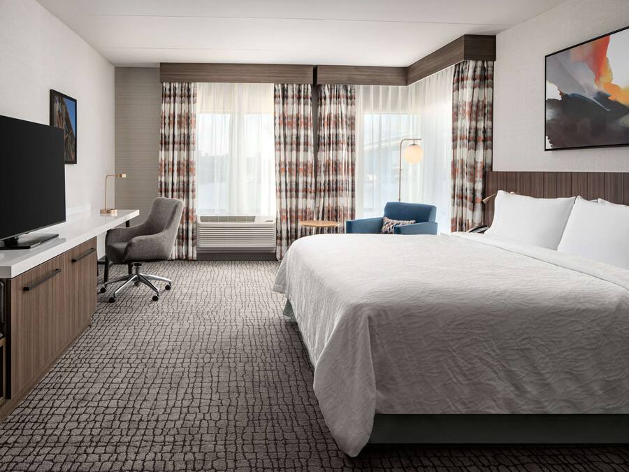 Une chambre d’hôtel avec un grand lit, un bureau doté d’un téléviseur à écran plat, une chaise et une fenêtre avec des rideaux.