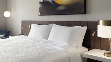 A neatly made bed with white linens, a modern bedside table with a lamp, and a large abstract painting on the wall.