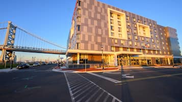 Um hotel moderno com uma entrada ampla, estacionamento e uma ponte ao fundo.