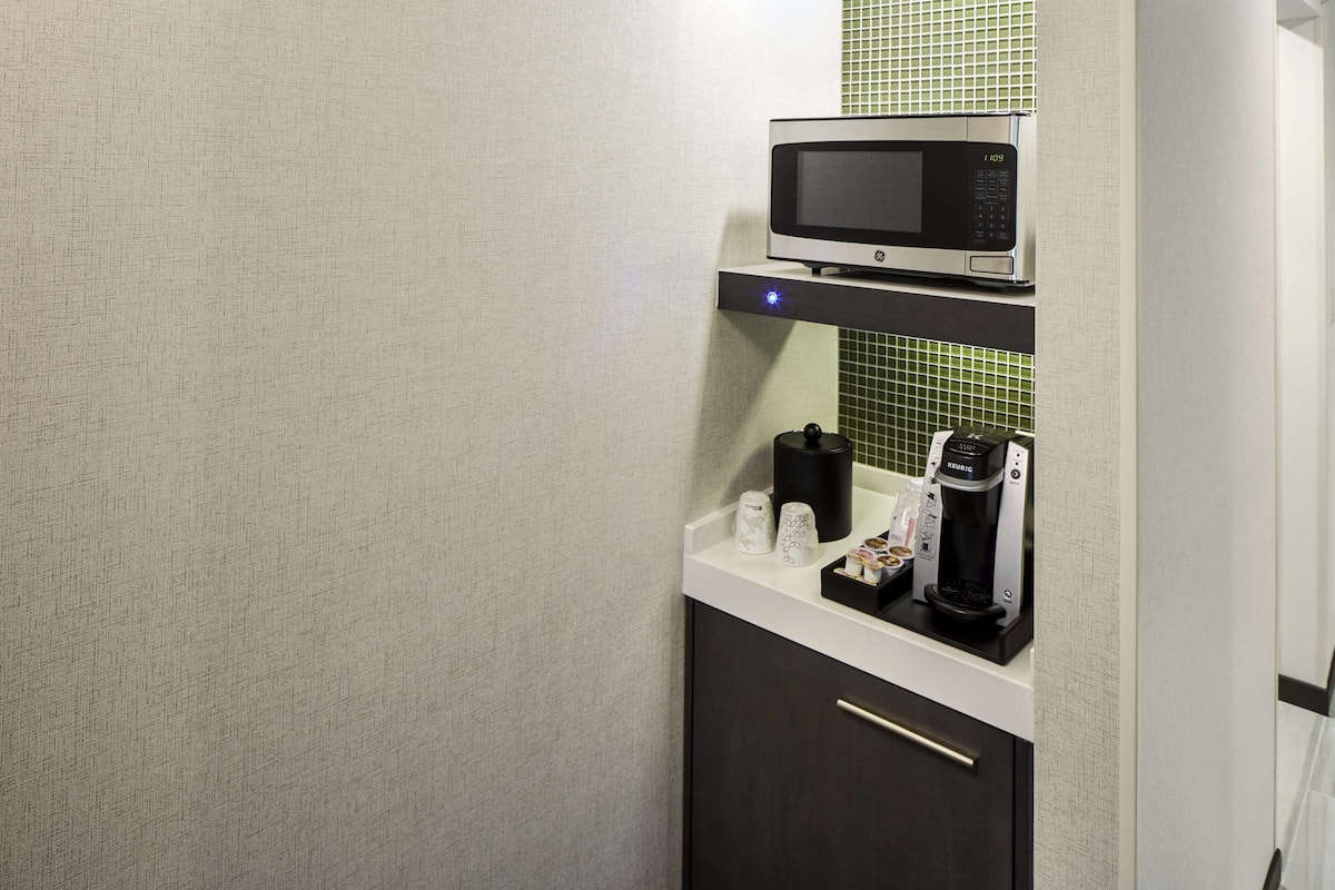 A kitchenette with a microwave, coffee maker, and cups on the counter.