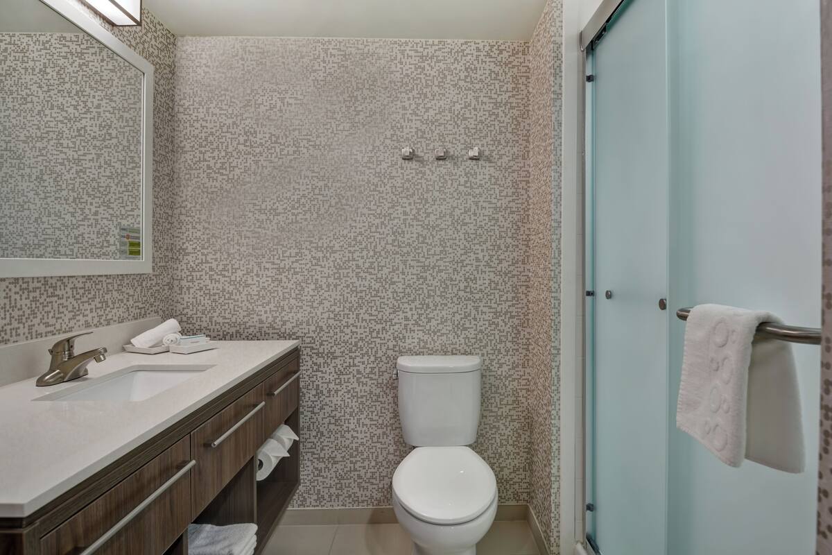 Une salle de bain avec un mur à motifs, des toilettes blanches, un lavabo avec un miroir et un porte-serviettes.