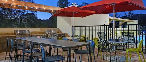 An outdoor patio with a barbecue grill, tables, chairs, and string lights.