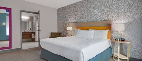 A hotel room with a large bed, a bedside table with a lamp, and a bathroom visible through an open door.