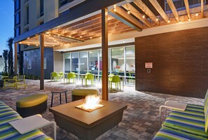 An outdoor seating area with a fire feature, green chairs, and a covered patio. - Home2 Suites by Hilton Largo (Largo)