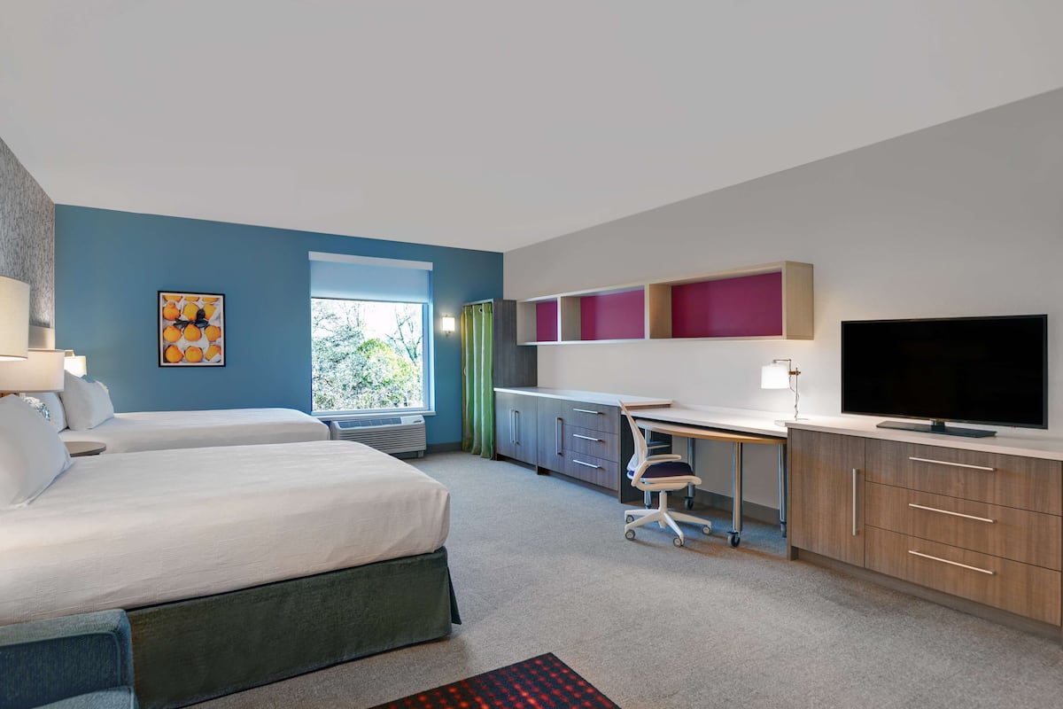Une chambre d’hôtel avec deux lits, un bureau, une télévision et une fenêtre avec des rideaux.