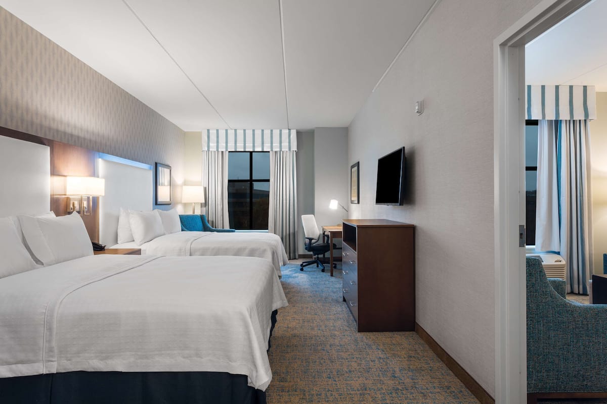 A hotel room with two beds, a desk, a chair, a TV, and a window with curtains.