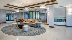 Eine großzügige Lobby mit einer zentralen Sitzecke, einem Kamin und einem modernen Deckenstil.