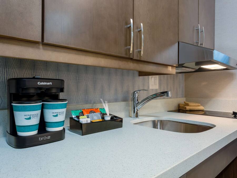 Eine Küchenzeile mit einer Cuisinart-Kaffeemaschine, zwei Papierbechern, einem Pod-Halter und einem Spülbecken.
