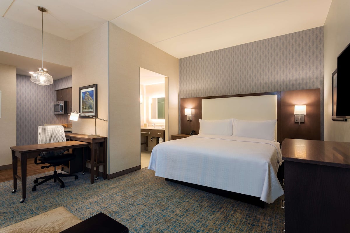 A hotel room with a bed, desk, chair, lamp, and a television.