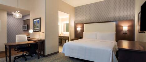 A hotel room with a bed, desk, chair, lamp, and a television.