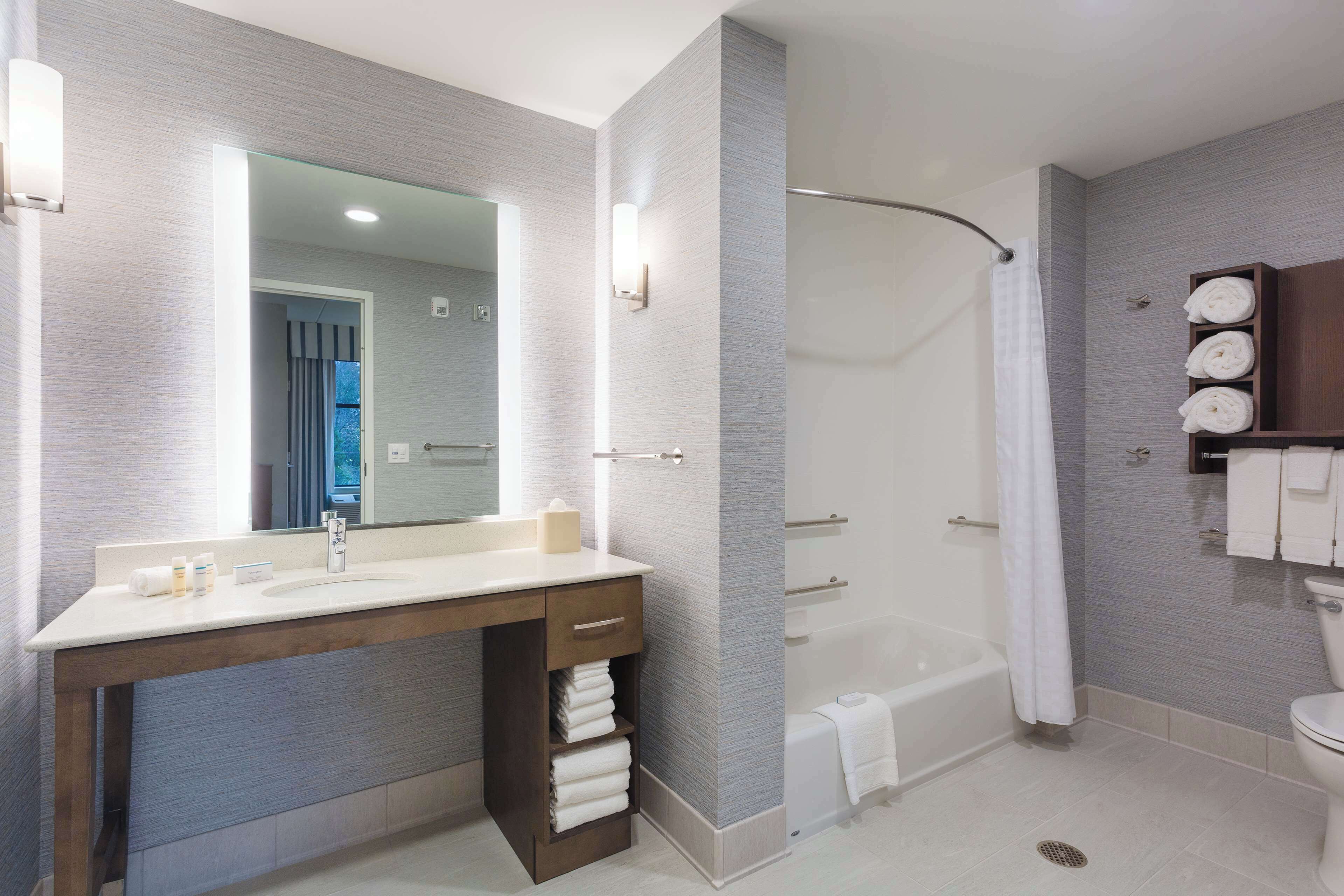 Un baño moderno con un espejo grande, un tocador de madera, una bañera y un inodoro.
