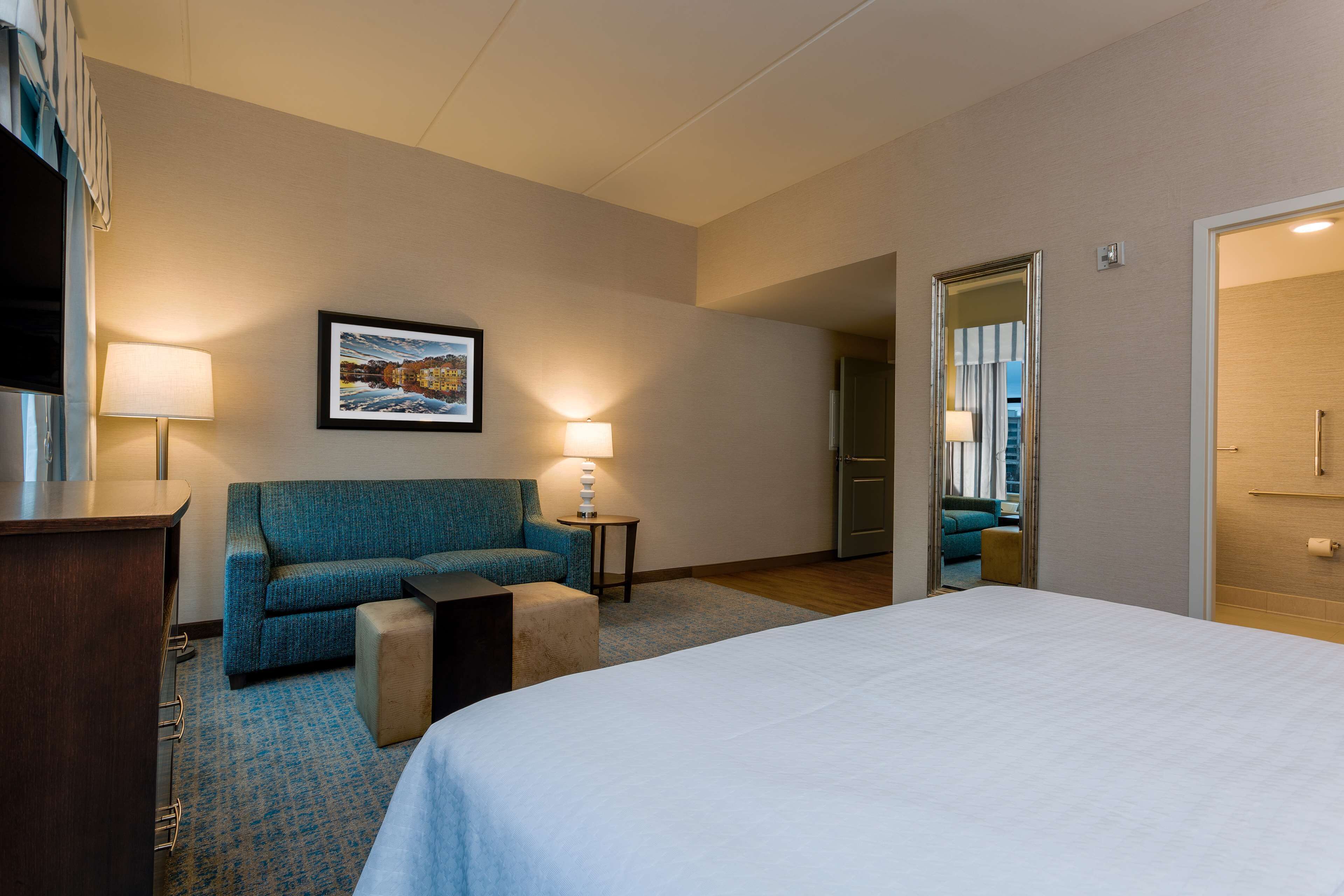 A hotel room with a bed, a sofa, a small table, a lamp, and a framed picture on the wall.