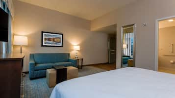 A hotel room with a bed, a sofa, a small table, a lamp, and a framed picture on the wall.