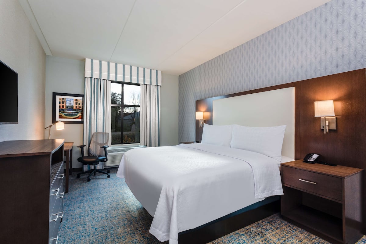 A hotel room with a large bed, a desk, a chair, and a nightstand with a phone.