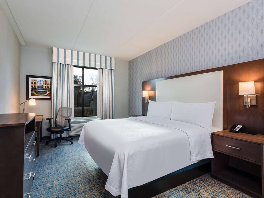 Habitación de hotel con una cama grande, un escritorio, una silla y una mesita de noche con teléfono.