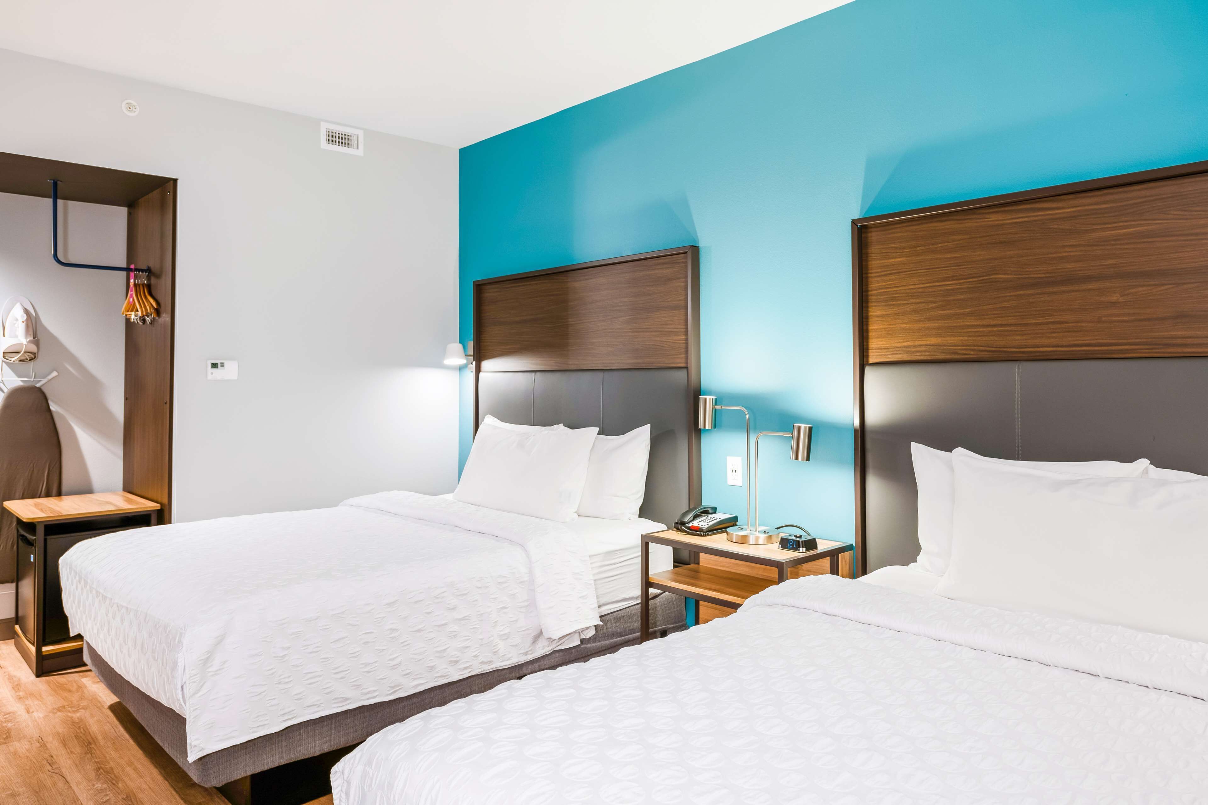 Habitación de hotel con dos camas, cabeceros de madera, ropa de cama blanca y mesitas de noche con lámparas y teléfonos.
