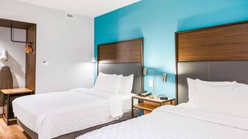 Habitación de hotel con dos camas, cabeceros de madera, ropa de cama blanca y mesitas de noche con lámparas y teléfonos.