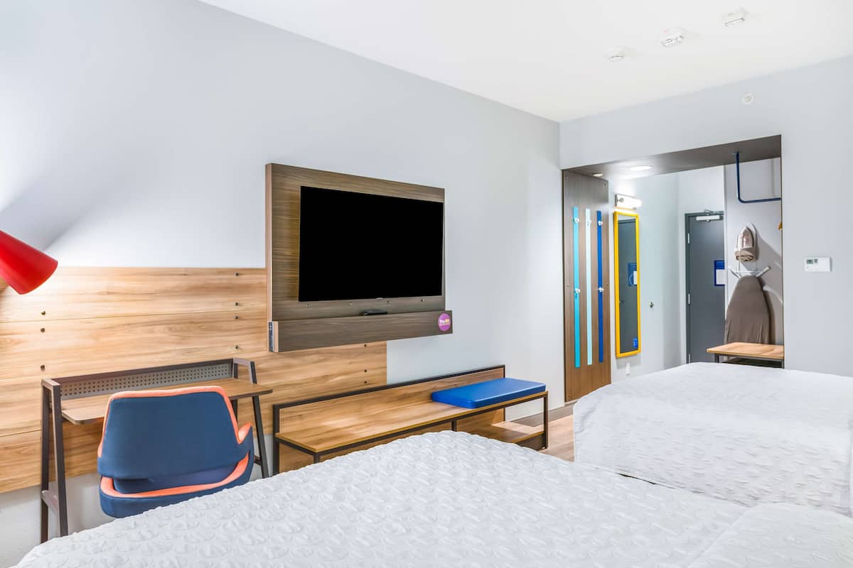 A hotel room with a bed, a desk, a chair, a TV mounted on the wall, and a bathroom visible through an open door.