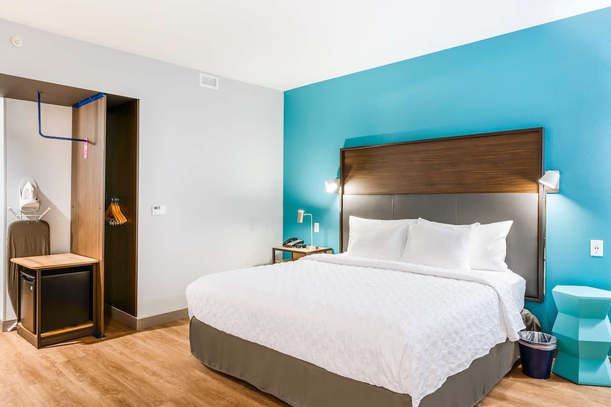A hotel room with a bed, a nightstand, a desk, a chair, a wardrobe, and a trash bin.