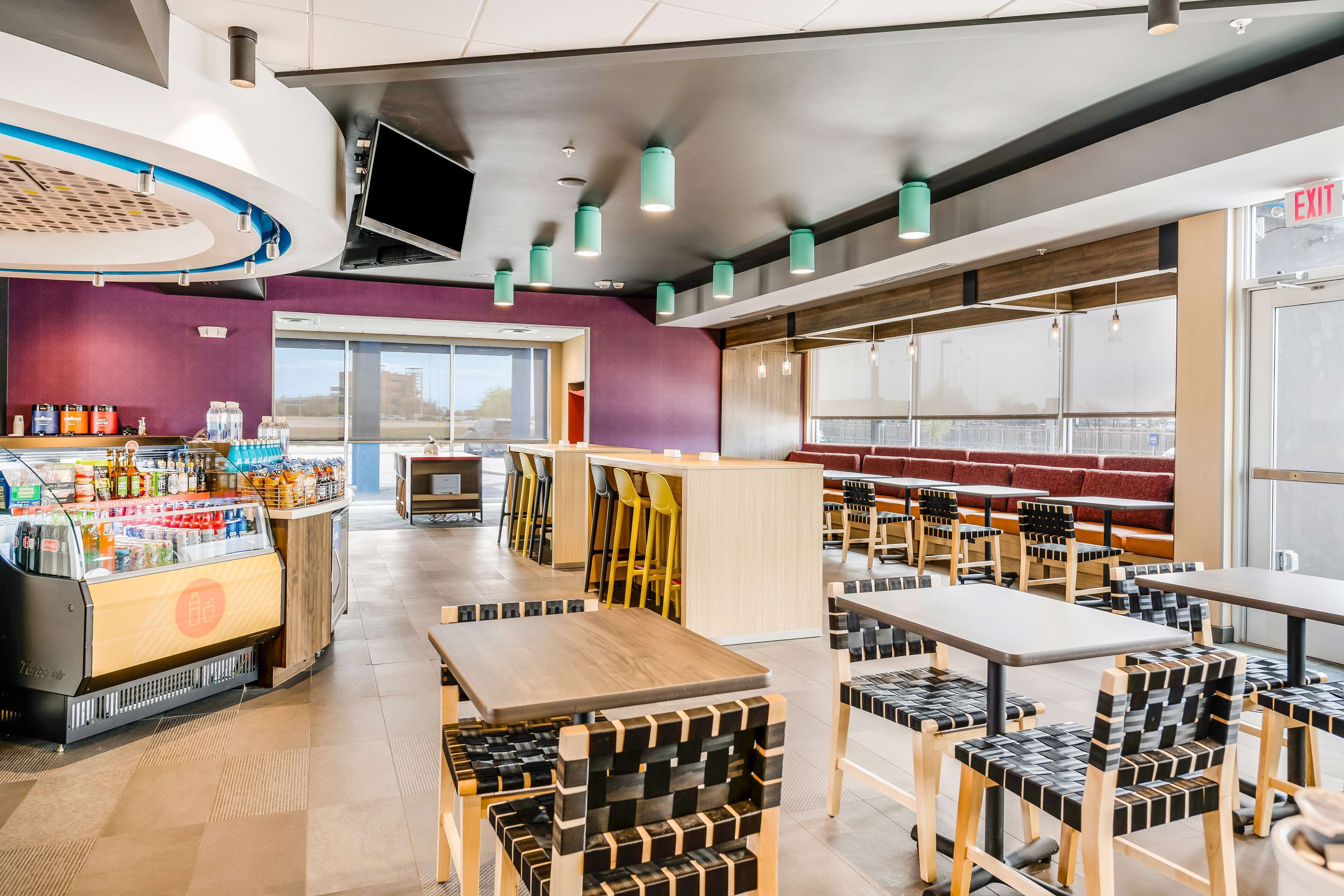Un café moderno con una estación autoservicio para bebidas, varias zonas de estar y vistas a la ciudad a través de grandes ventanales.