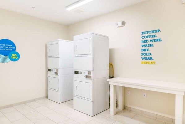 Un lavadero con dos lavadoras y secadoras apiladas, una mesa blanca y una pared con un cartel de instrucciones para la ropa.