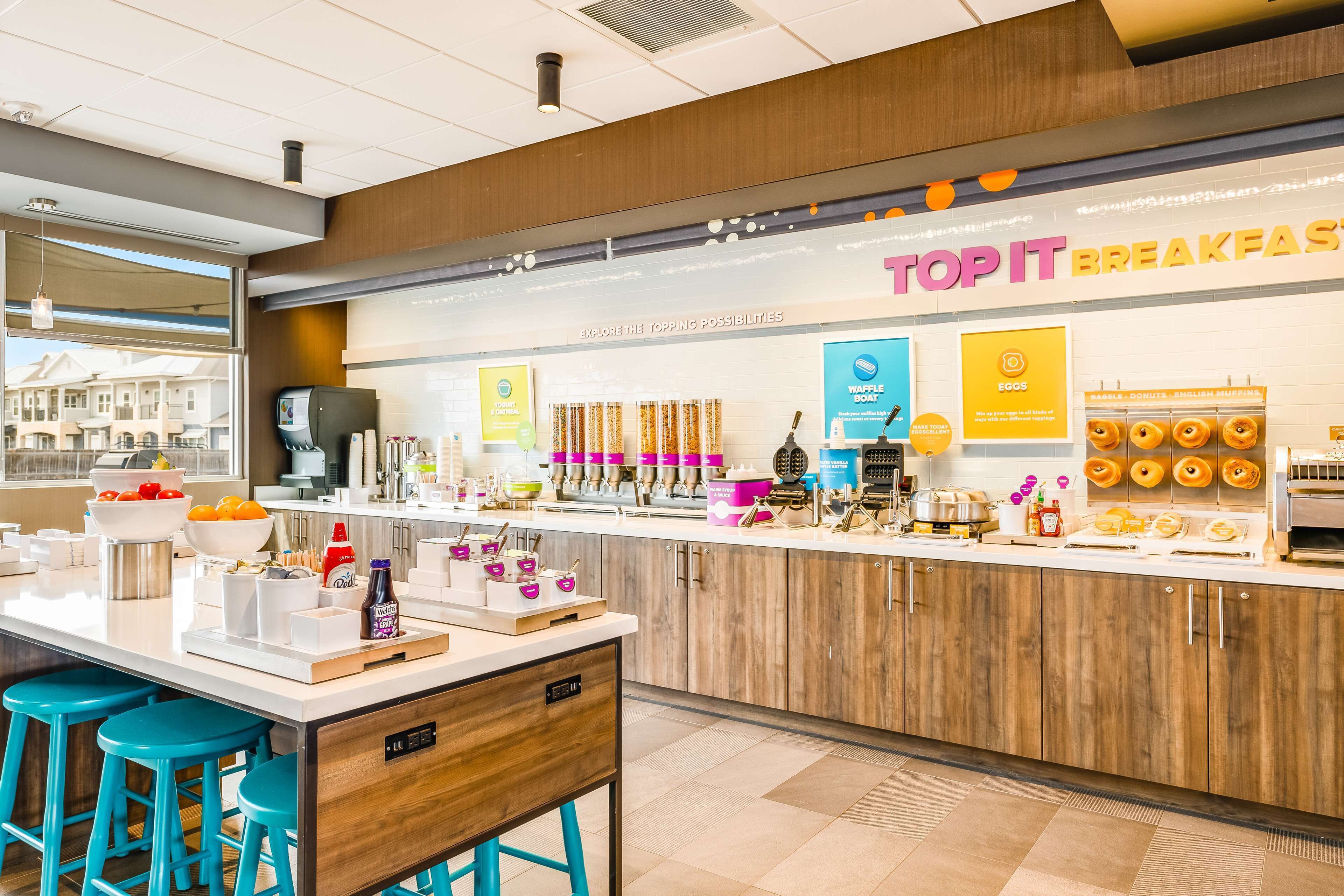 A modern breakfast area with a counter displaying various food items and a sign reading "TOP IT BREAKFAST".