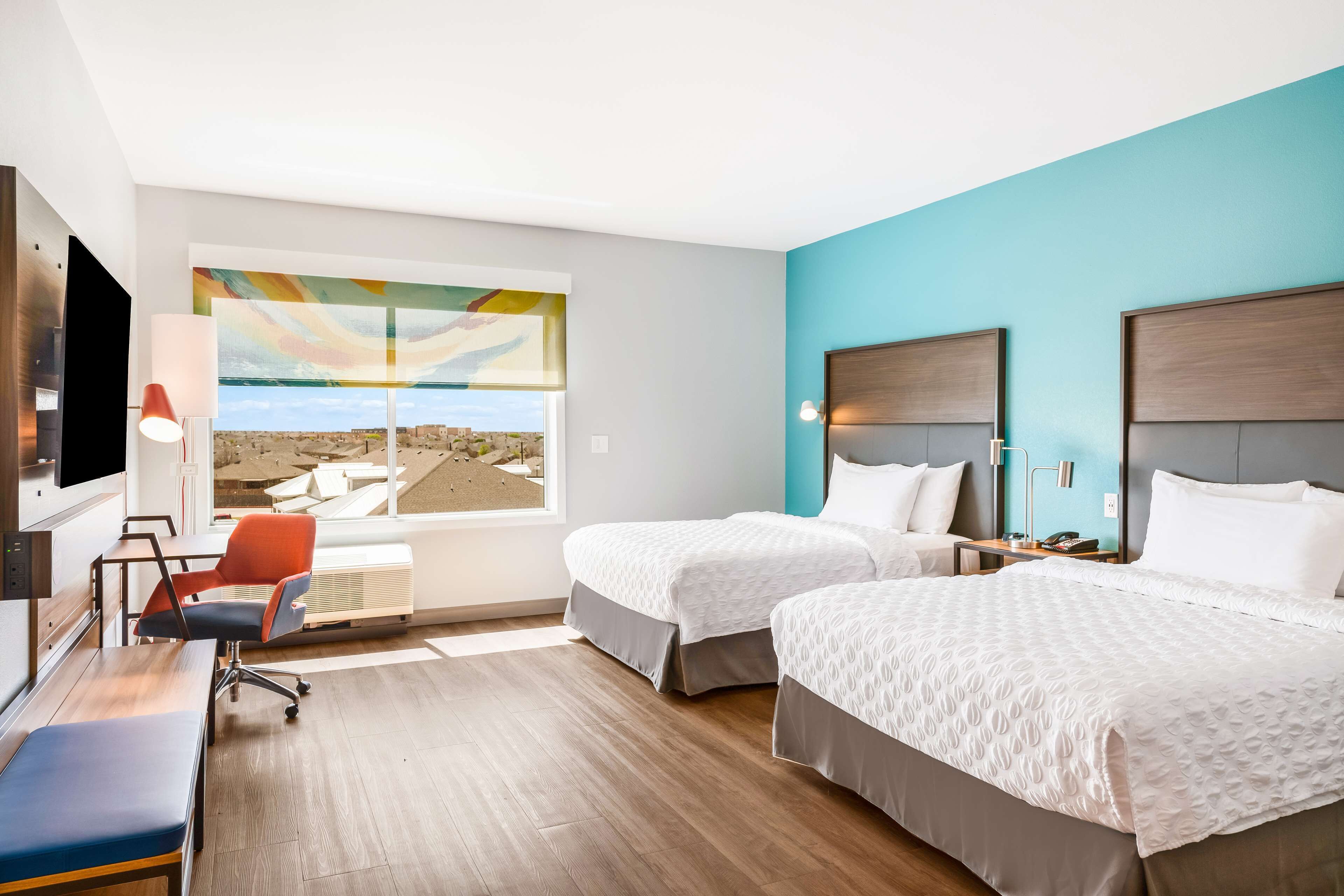 Habitación de hotel con dos camas, un escritorio, una silla y un ventanal con vistas.