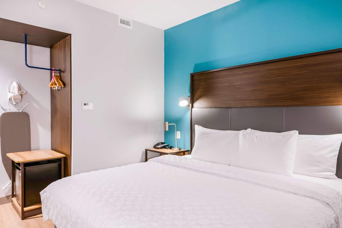 A hotel room with a large bed, a wooden nightstand, a desk with a lamp, and a blue accent wall.