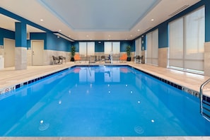 A large indoor swimming pool with clear lane markings, a lifeguard chair, and lounge chairs along the poolside.