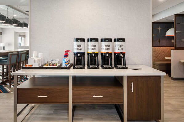 Un espace dédié au café, équipé de quatre distributeurs de café étiquetés « Mélange corsé », « Mélange léger », « Décaféiné » et « Eau chaude ».