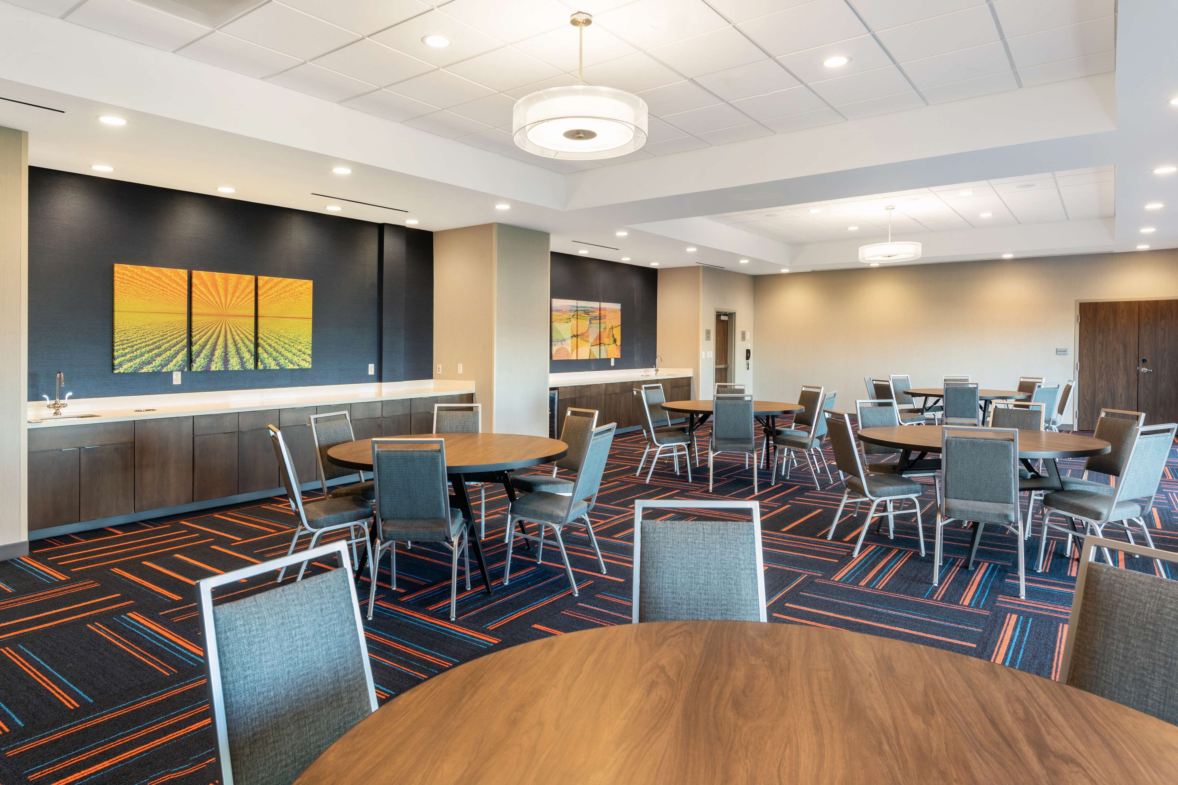 A modern conference room with round tables and chairs, a patterned carpet, and artwork on the walls.