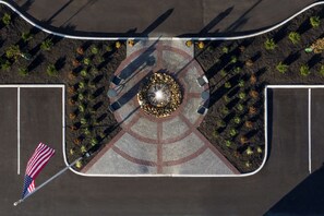 An aerial view of a parking lot with a circular landscaped area, a flagpole with an American flag, and a paved road curving around the lot.