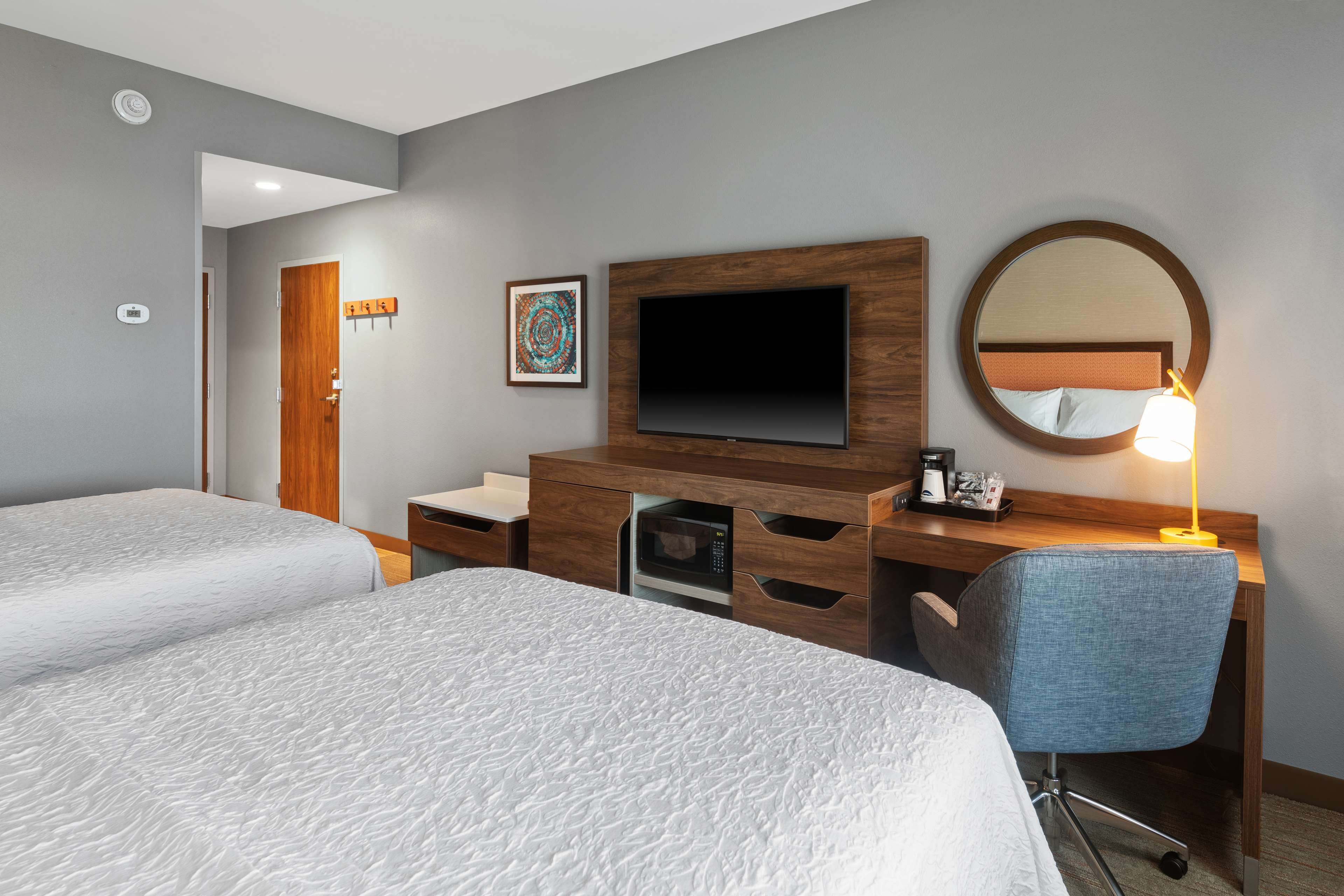 A hotel room with two beds, a TV, a desk with a lamp, a microwave, and a mirror.