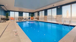 A modern indoor pool with clear blue water, large windows, and a view of a city skyline. - Hampton Inn Circleville (Circleville)
