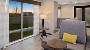 A modern hotel room with a large window, a sofa with a yellow pillow, a small round table, and a floor lamp. - Hampton Inn Circleville (Circleville)