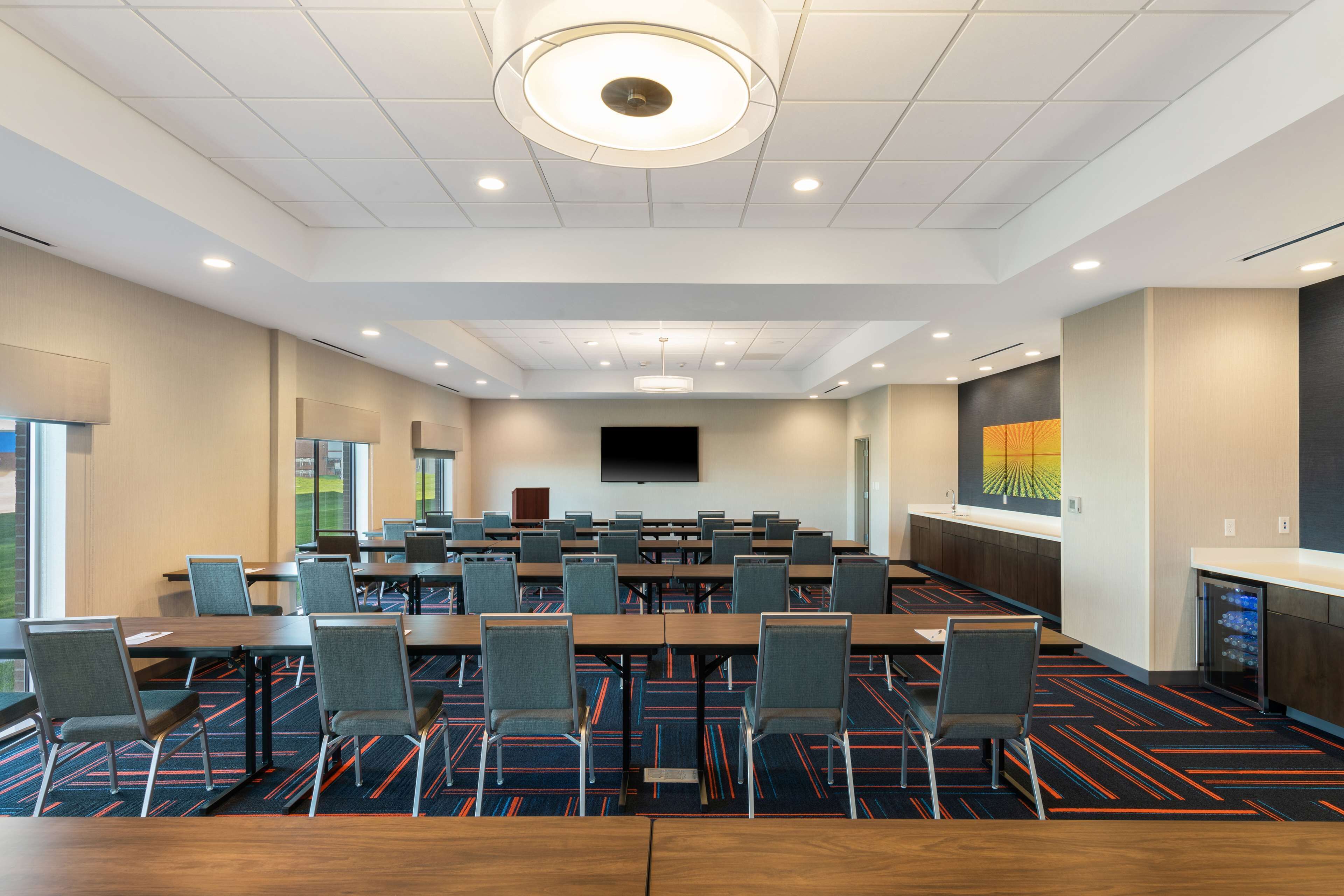 A conference room with multiple tables and chairs, a large flat-screen TV, and a carpeted floor.