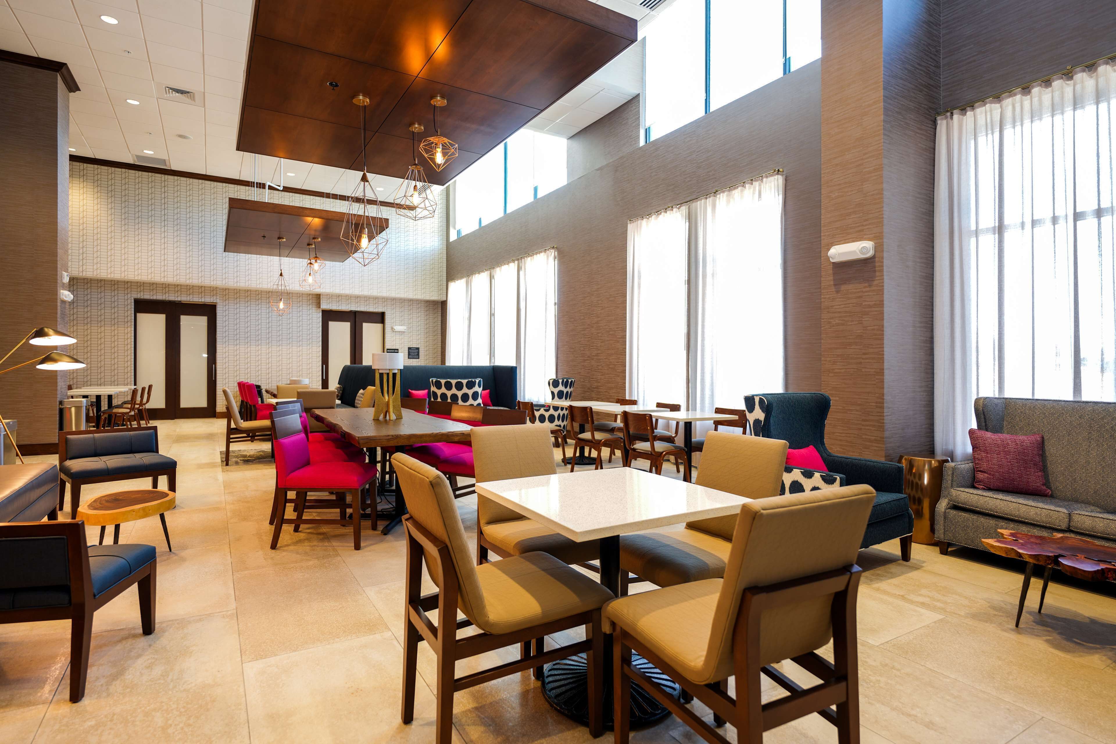 A spacious hotel lobby with high ceilings, large windows, and a variety of seating options including tables, chairs, and sofas.
