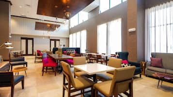 A spacious hotel lobby with high ceilings, large windows, and a variety of seating options including tables, chairs, and sofas.