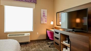 A hotel room with a bed, a desk with a chair, a television, a heater, and a window with blinds.