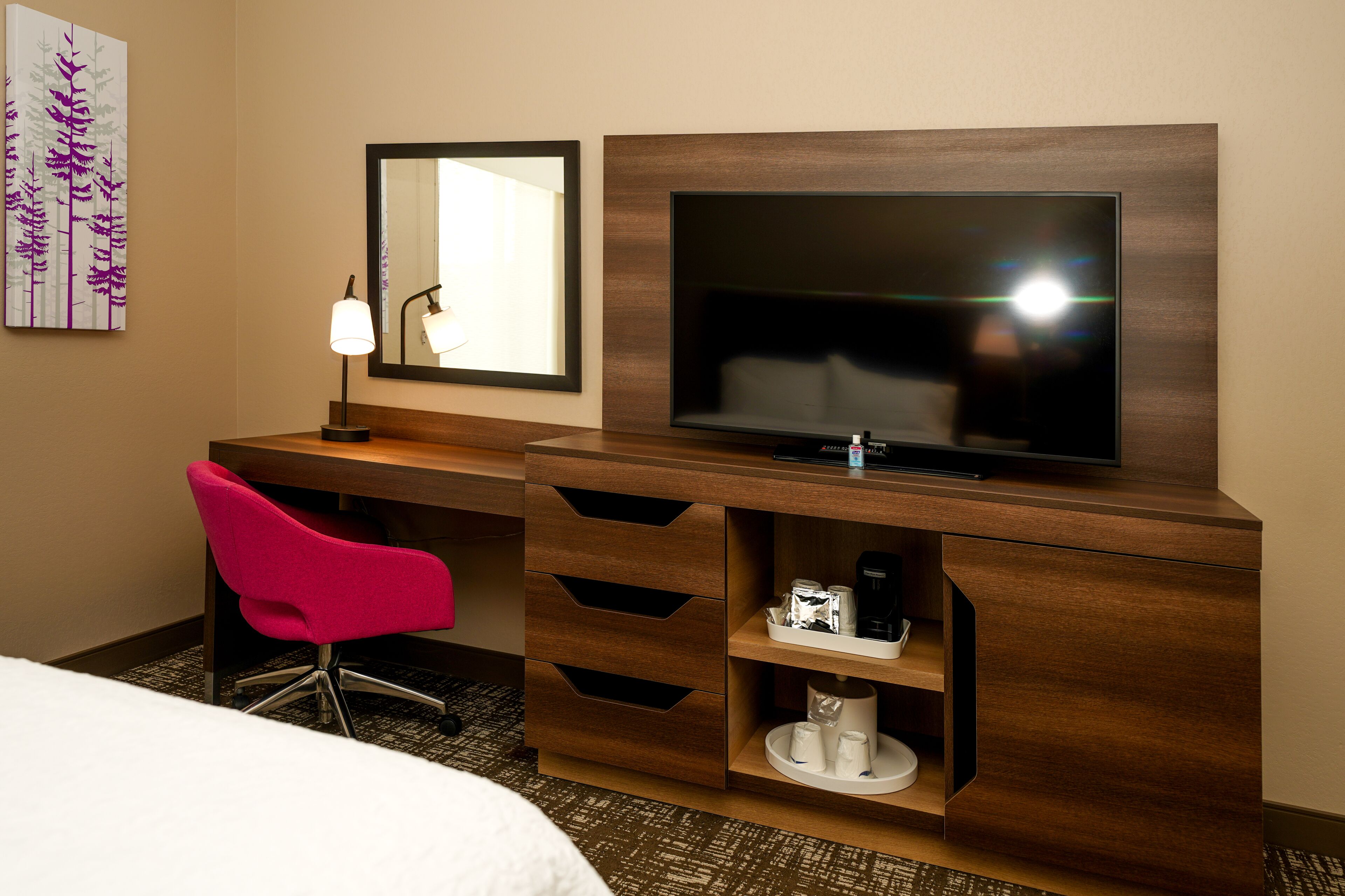 A hotel room with a wooden desk, a television, a pink chair, and a bed.