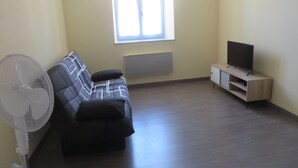 A living room with a sofa, a standing fan, a TV on a wooden stand, and a window with blinds. - 4 to 6 berth accommodation 10 mi walk from the lake (Clairvaux-les-Lacs)