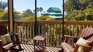 A wooden deck with two Adirondack chairs and a small table, overlooking a coastal area with houses and palm trees. - Little Gasparilla Island Getaway (Placida)