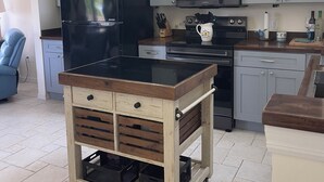 A kitchen with a black refrigerator, a microwave, and a stove. There are framed pictures on the wall and a blue chair in the corner. - Little Gasparilla Island Getaway (Placida)