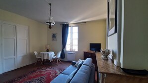 A living room with a sofa, a small table with chairs, a television, and a decorative vase. - Large charming studio (Cordes-sur-Ciel)