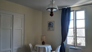 A dining area with a table and two chairs, a ceiling fan, a window with curtains, and a radiator. - Large charming studio (Cordes-sur-Ciel)