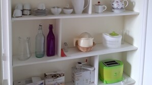 A white shelving unit with various kitchen items, including cups, bowls, and a green toaster. - Large charming studio (Cordes-sur-Ciel)