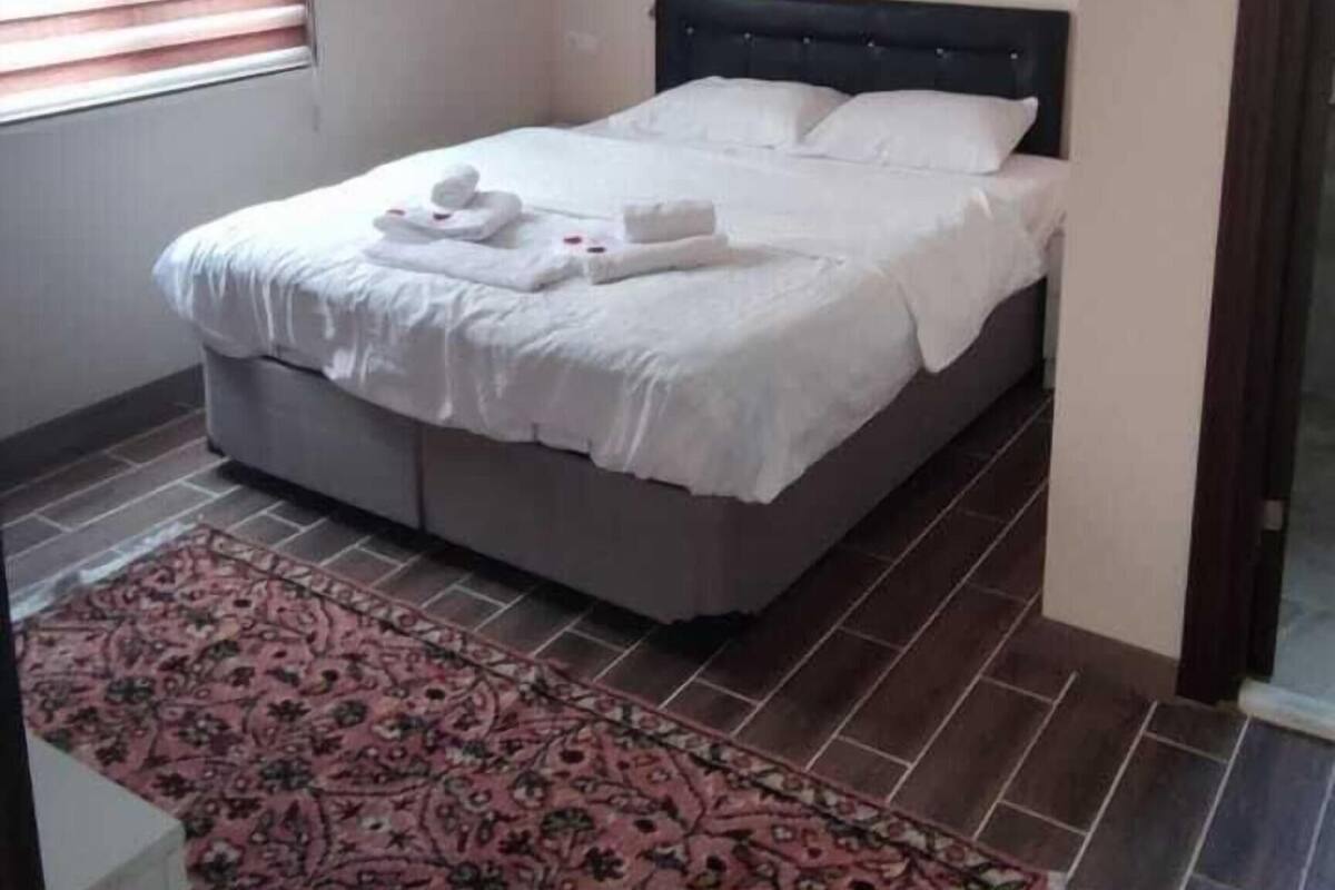 A bedroom with a bed, a ceiling light fixture, a window with blinds, and a patterned rug.