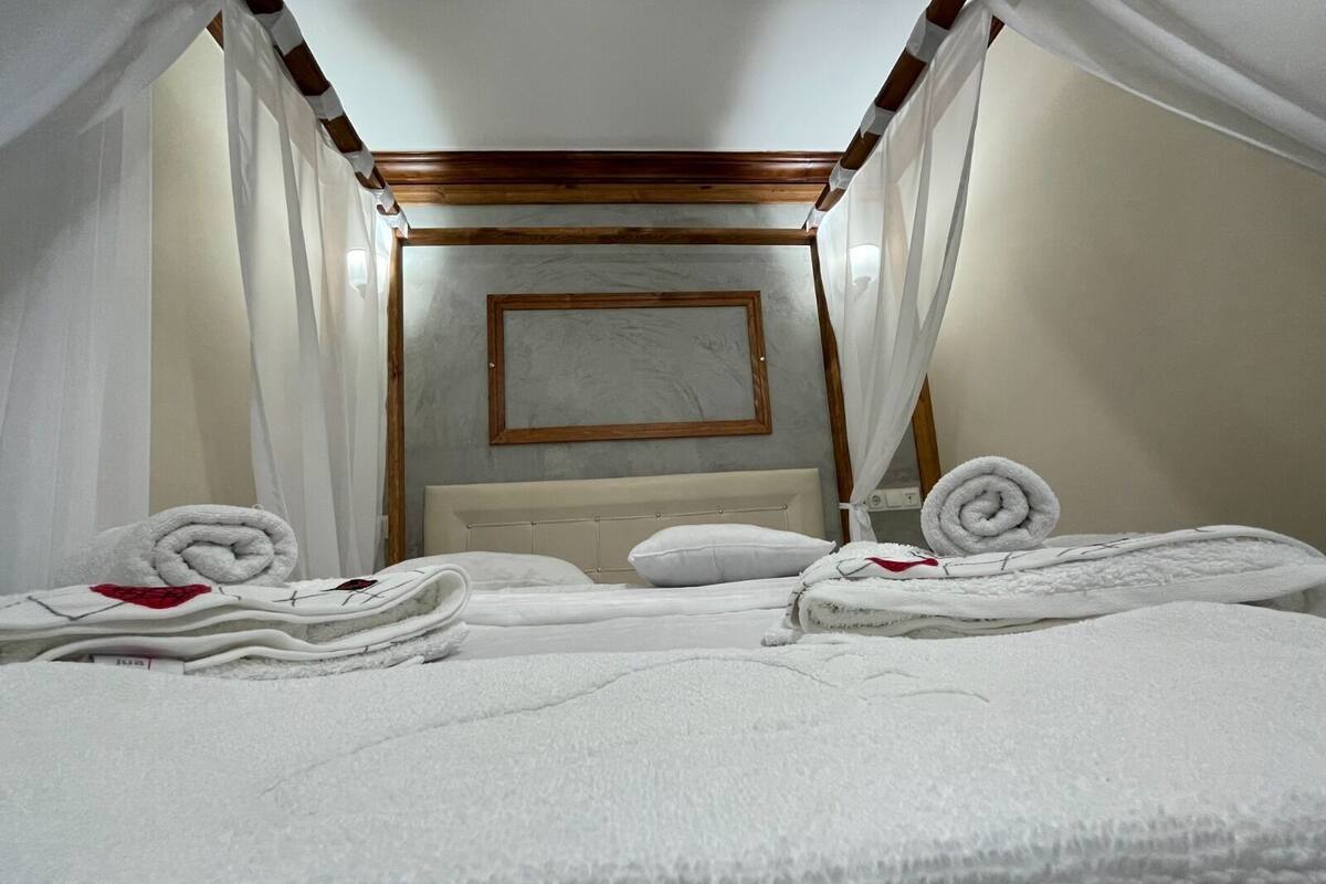 A hotel room with two beds, white linens, a wooden headboard, a framed picture on the wall, and a canopy bed.